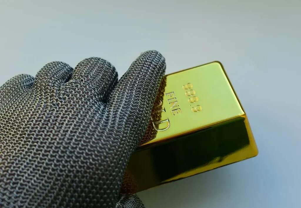 Close-up-of-a-metal-gloved-hand-holding-a-shiny-gold-bar-indoors
