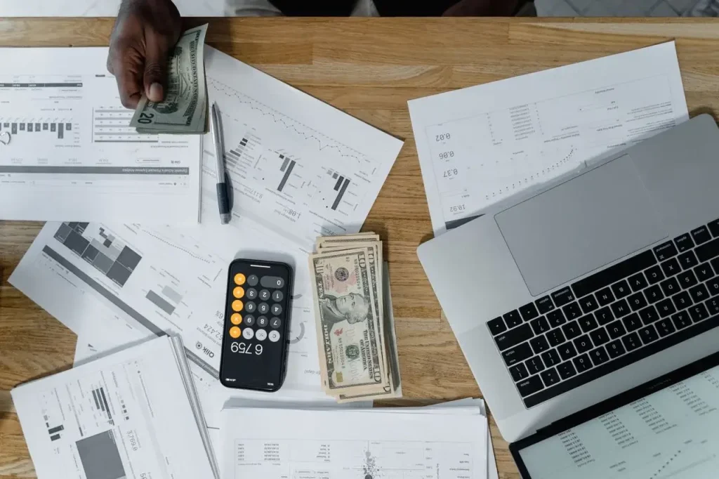 Overhead view of a busy workspace with cash, financial documents, and a laptop image