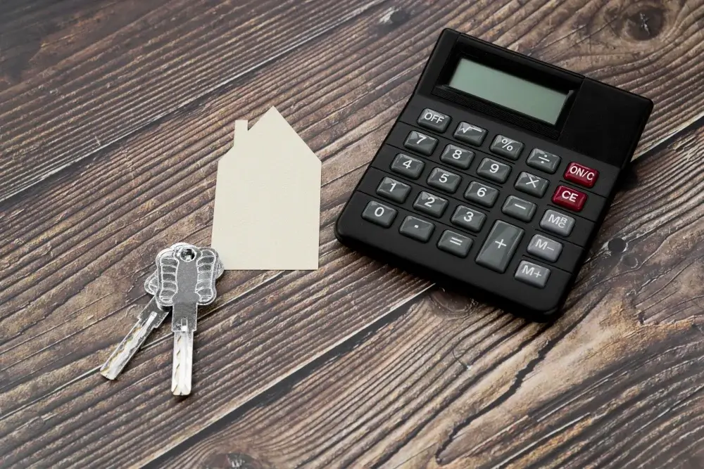 Paper-cut-out-house-with-keys-and-calculator-on-wooden-textured-surface